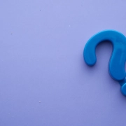 Un symbole de point d'interrogation en plastique bleu sur fond violet clair, créant un int
